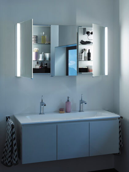 Waschplatz beleuchtet mit geöffetem Spiegelschrank und einem Doppelwaschbecken.