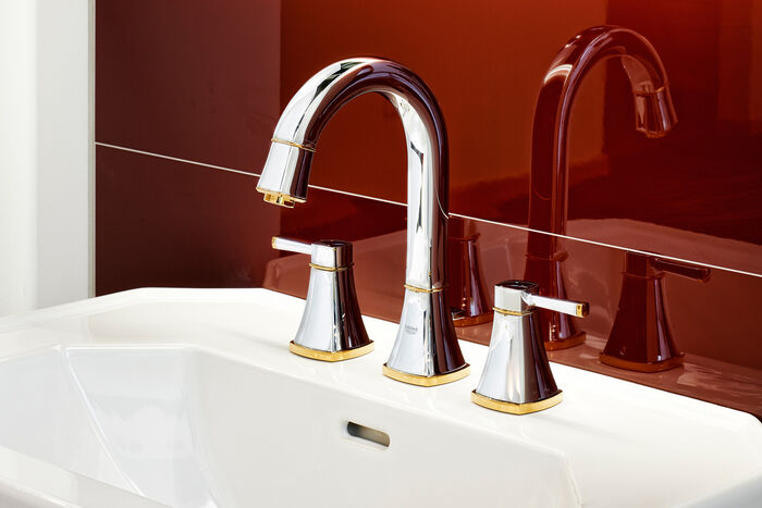 GROHE Grandera™ Edles Waschbecken, an dem Frohe Grandera Badarmaturen befestigt sind. Im Hintergrund glänzen rote Fliesen.