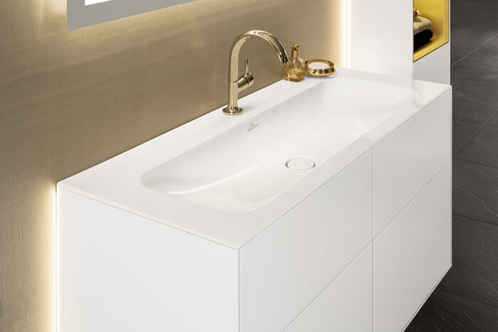 Waschbecken weiß mit goldener Badarmatur und Unterschrank.