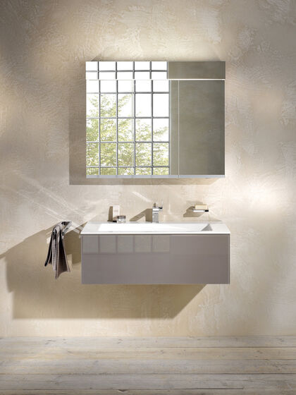 Waschbecken Edition 11 von Keuco, das an einer beigen Wand installiert ist. Auf dem Waschbecken stehen Hygieneartikel, darüber hängt ein Spiegel.