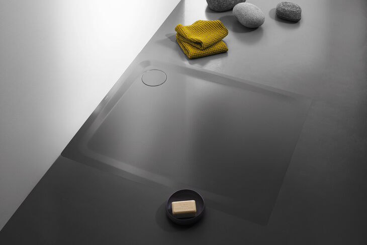 Schwarze, rutschfeste und bodenebene Kaldewei Secure Plus Duschfläche, die in einem schwarzen Boden eingelassen ist. Daneben liegen gelbe Handtücher.