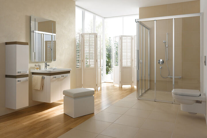 Komfort Badezimmerambiente mit begehbarer Dusche, wandmontierter Toilette und gegenüber ein Waschplatz mit Spiegel, einem Hochschrank und Hocker.