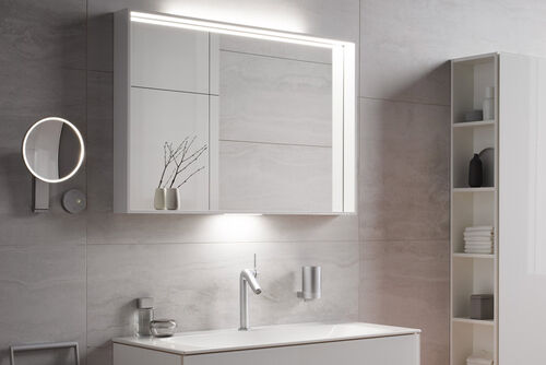 Kosmetikspiegel und Spiegelschrank beleuchtet an Waschplatz mit hellen Badmöbeln.