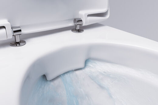 WC Rimfree® von Geberit mit neuester, spülrandloser Technologie. Einblick in das WC-Becken, wo blau eingefärbtes Spülwasser sich gleichmäßig im Becken verteilt.