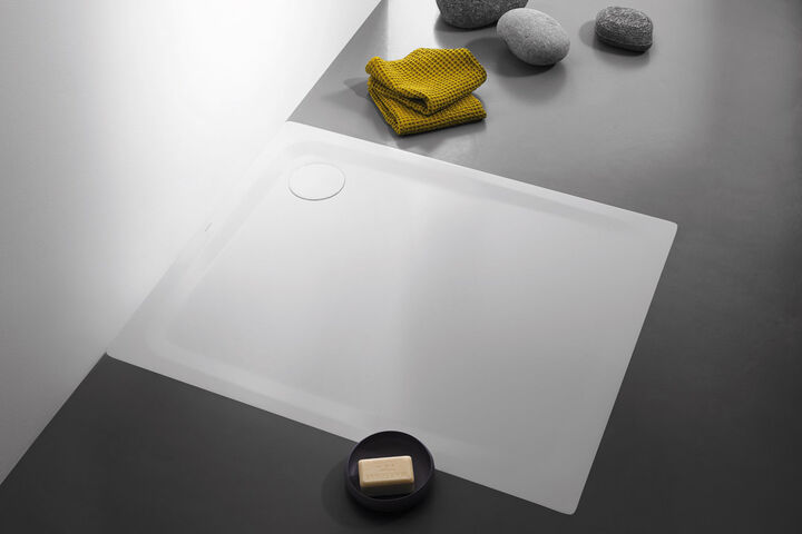 Weiße, rutschfeste und bodenebene Kaldewei Secure Plus Duschfläche, die in einem schwarzen Boden eingelassen ist. Daneben liegen gelbe Handtücher.