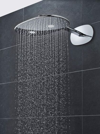 GROHE Smart Control Duschkopf, der an einer schwarz-grau gefliesten Badezimmerwand befestigt wird. Aus der Kopfbrause fließt Wasser.