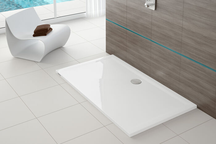 Eine weiße Hoesch-Duschfläche, die Design und Komfort verbindet. Im Hintergrund liegen braune Handtücher auf einer weißen Sitzgelegenheit.