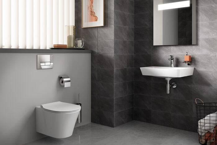 Bad mit wandmontierter Toilette an grauer Wand und einem Waschbecken mit Armatur.