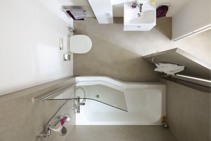 Von oben fotografiertes kleines Badezimmer mit einr Badewanne an der Wand, toilette, Hochschrank und Waschplatz.