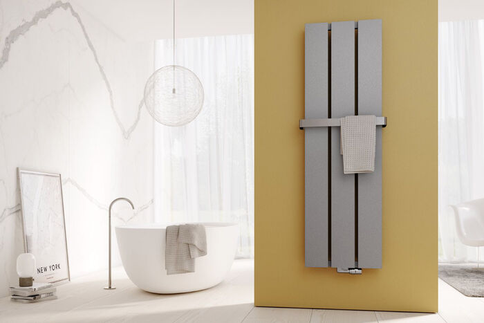 Moderner Badheizkörper Dekor-Arte Plan von Kermi in Stahloptik mit Handtuchbügel vor ockerfarbener Wand in Badezimmer mit Freistehwanne.