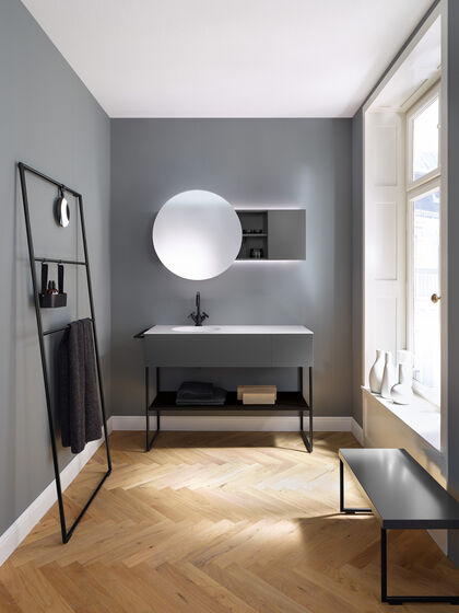Modernes puristisches Badezimmer mit grauen Badmöbeln. Spiegelschrank mit rundem Spiegel zum Verschieben. Waschbecken rund eingebaut und seitlich eine Sitzbank.