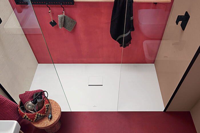 Hautsympathische, weiße Acryl-Duschwanne der Serie Collaro von Villeroy & Boch in rechteckig mit Ablauf in der Mitte, mit einer roten Rückwand an der Dusche.