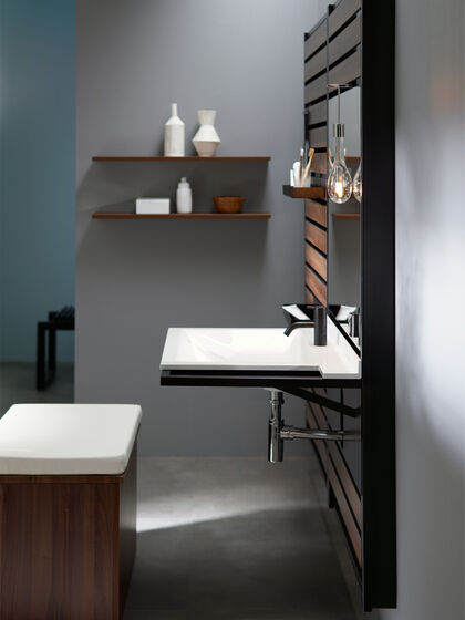 Detailbild eines Waschplatzes von burgbad Flex: Der Waschtisch ohne Unterschrank kann mit dem gepolstertem Rollcontainer als Sitzgelegenheit im Sitzen genutzt werden. Dunkles Ambiente und dunkelbraunes Holzdekor.
