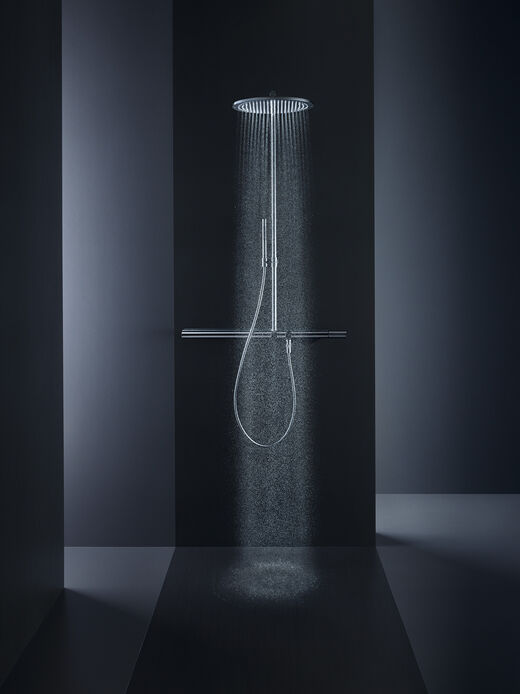 AXOR Showers Schwarzer, eleganter Raum, in dem eine Axor Showers Kopfbrause installiert ist. Das Wasser fließt aus der Brause, geheimnisvolles Licht bringt den Raum in eine besondere Athmosphäre.
