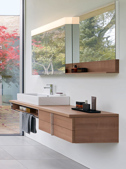 Duravit Vero Seitenansicht auf einen edlen Waschplatz von Duravit Veröffentlicht mit Waschbecken, Unterschränken und Spiegelschrank mit Beleuchtung.