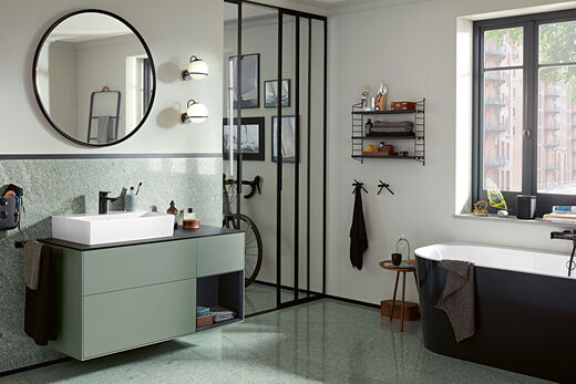 Modernes City-Badezimmer mit klaren Linien und Formen: runder Spiegel trifft auf rechteckiges Badmöbel von Villeroy & Boch, gekrönt von einem edlen Keramikwaschtisch der Serie Memento 2.0. Außerdem Fahrrad und Badewanne.