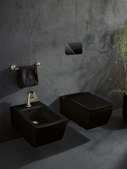 Black in Black - coole Szene mit schwarzer Bidet und Toilette aus der Serie Memento 2.0, der runderneuerten Keramiklinie von Villeroy & Boch vor einer dunkelgrauen Wand und mit goldenen Armaturen veredelt.