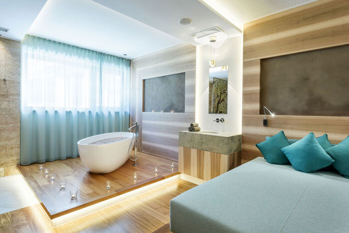 Grosse Spa suite mit freistehender Badewanne und begehbarer Dusche. Helle Holzmöbel und blaue Überzüge für das Bett.