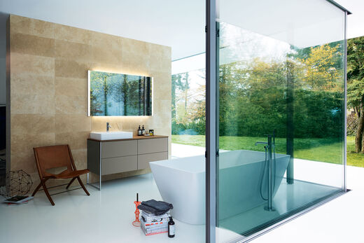 Duravit Square Großes Badezimmer mit freistehender Badewanne und Waschplatz mit beigem Unterschrank und beleuchteter Spiegel.