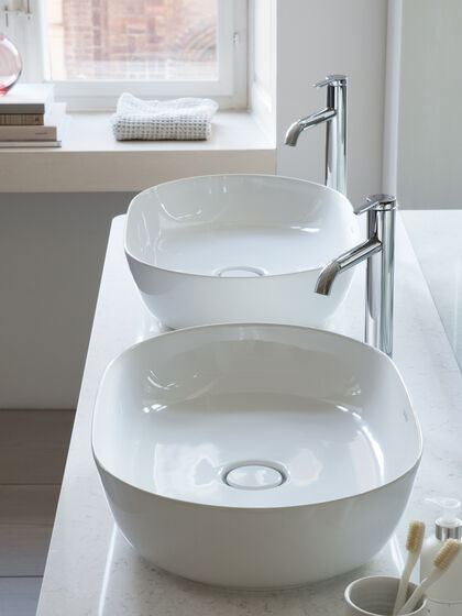 Zwei Aufsatzwaschbecken oval auf weißem Badmöbel mit Standarmaturen in Chrom.