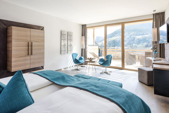 Suite mit Balkon Alpiana Resort. Wandmontierter holzschrank seitlich, Doppelbett, Flat-TV und Sessel.
