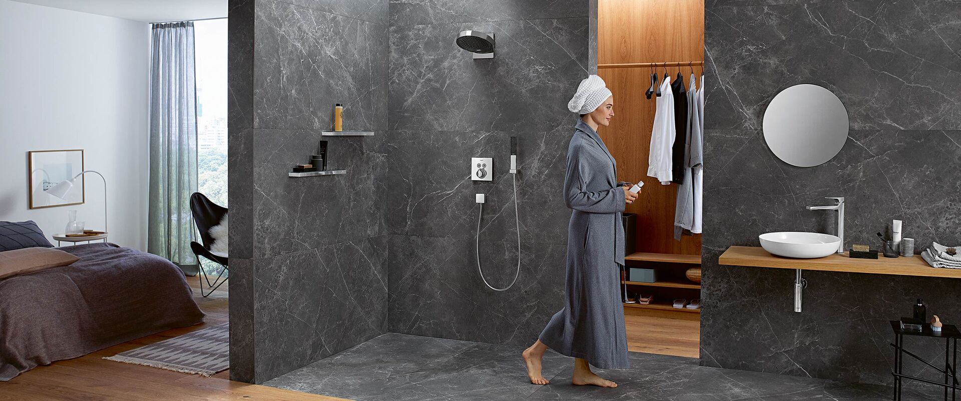 Frau verlässt die Dusche im Bademantel in einer modernen, offenen Badgestaltung mit den innovativen Brausen aus dem System Rainfinity von hansgrohe.