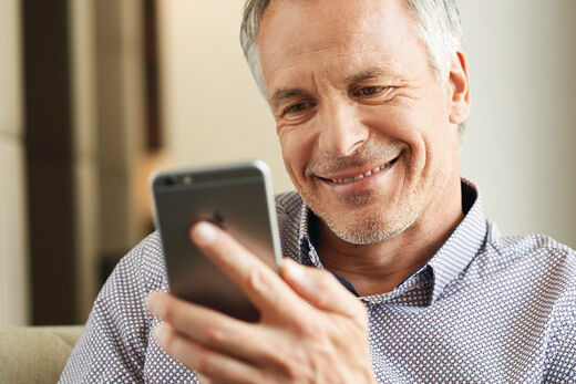 Mann mit violett-weiß kariertem Hemd tippt in sein Smartphone und lacht.