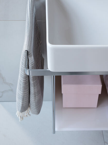 Handtuchhalter am Waschbecken in Chrom mit grauem Handtuch.