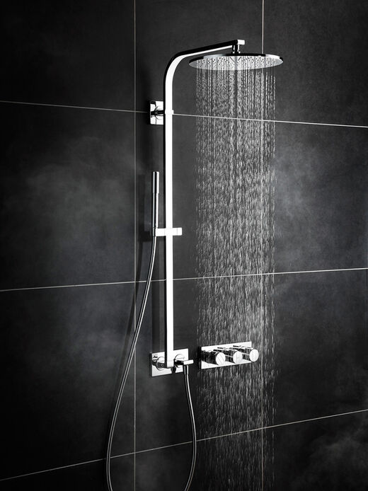 Ideal Standard Archimodule Dusche, in der an der schwarz gefliesten Wand Ideal Standard Archimodule Badarmaturen installiert sind.