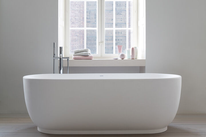 Exklusive große Badewanne, oval mit Standarmatur. Die Wanne steht vor einem Fenster.