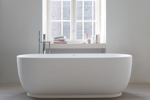 Exklusive große Badewanne, oval mit Standarmatur. Die Wanne steht vor einem Fenster.
