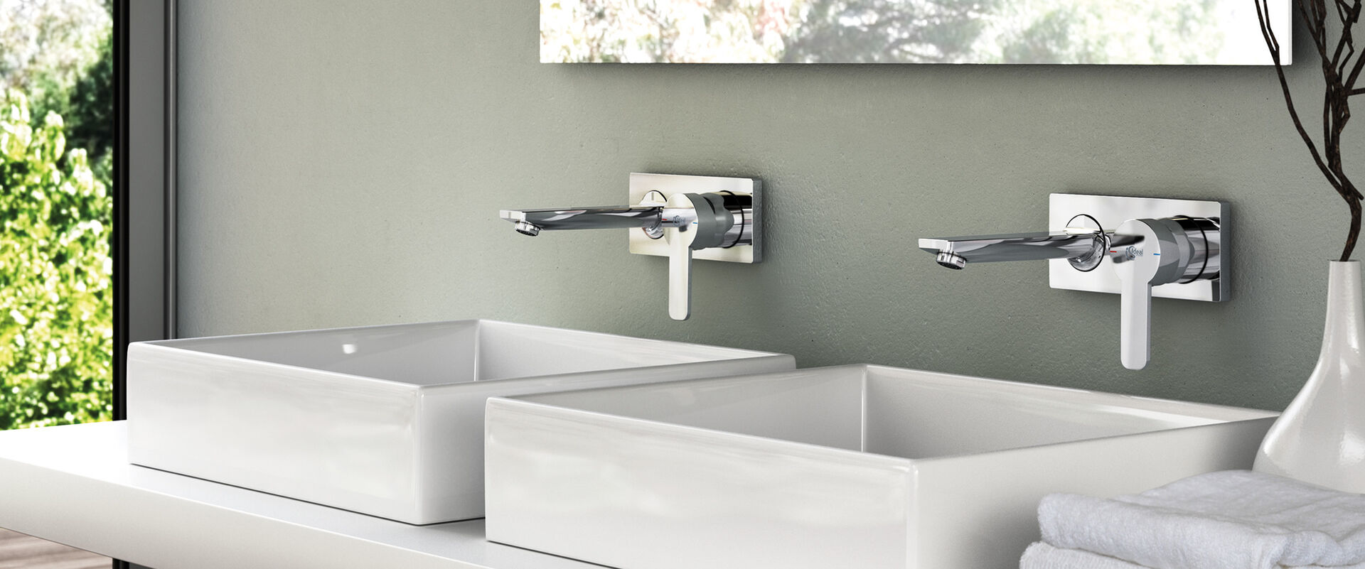 Waschtisch mit freistehenden Waschbecken, über denen 2 GIO Ideal Standard Wasserhähne installiert sind. Die Wand ist grün-grau gestrichen.