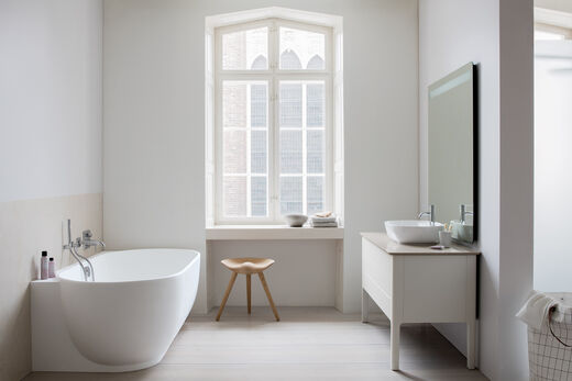 Ovale Badewanne, die an der Wand steht. Blick auf ein komplettes Badezimmer mit einem Waschtisch und Spiegel.