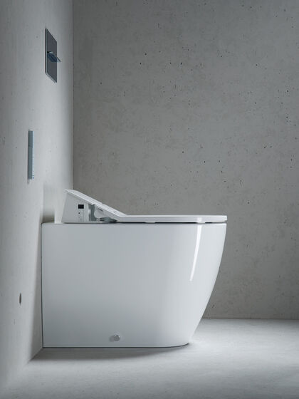 Seitenansicht des bodenstehenden Modells SensoWash von Philipe Starck, der für Duravit exklusiv die Serie der Dusch-WCs entworfen hat. Weißes Dusch-WC vor Betonwand.