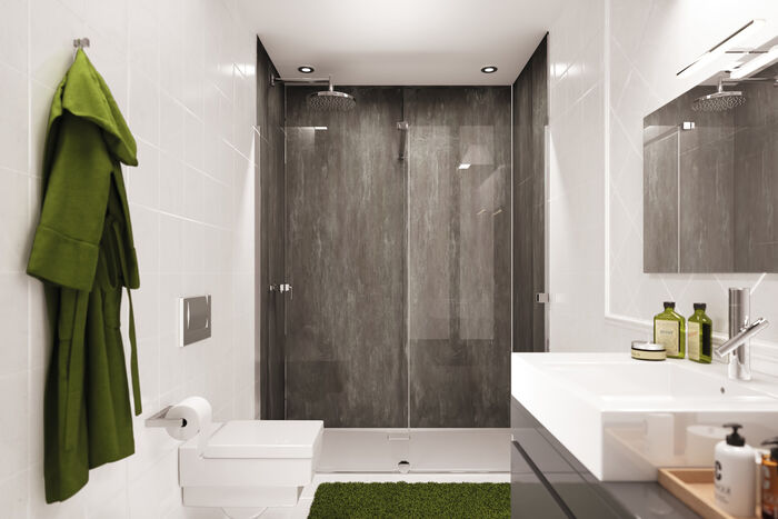 Badezimmer, in dessen Dusche eine dunkelgraue Easy Style Wandverkleidung von HUEPPE angebracht ist. vor der Dusche befindet sich Links eine Toilette, daneben hängt ein Bademantel. Rechts befindet sich ein Waschbecken mit Spiegel.