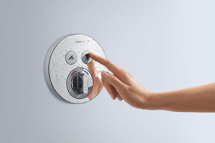 Shower Select Mixer von hansgrohe, in runder Form gehalten. Eine Hand betätigt den rechten Knopf des Thermostats.