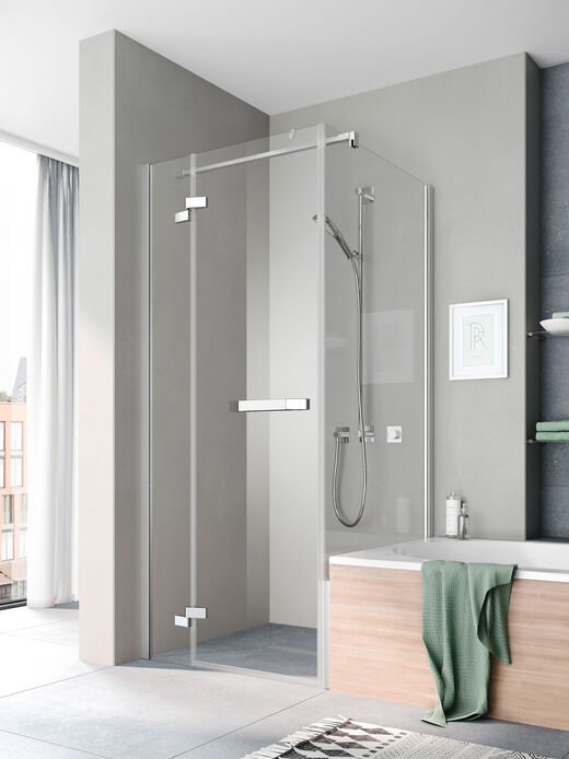 Kermi Tusca Duschkabine, die ein einem Badezimmer mit grauen Wänden installiert ist. Rechts davon befindet sich eine Badewanne, darüber liegt ein grünes Handtuch.