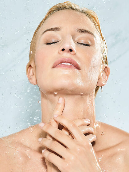 Frau hält sich die Hände vor den Hals und duscht vor weißer Marmorwand.