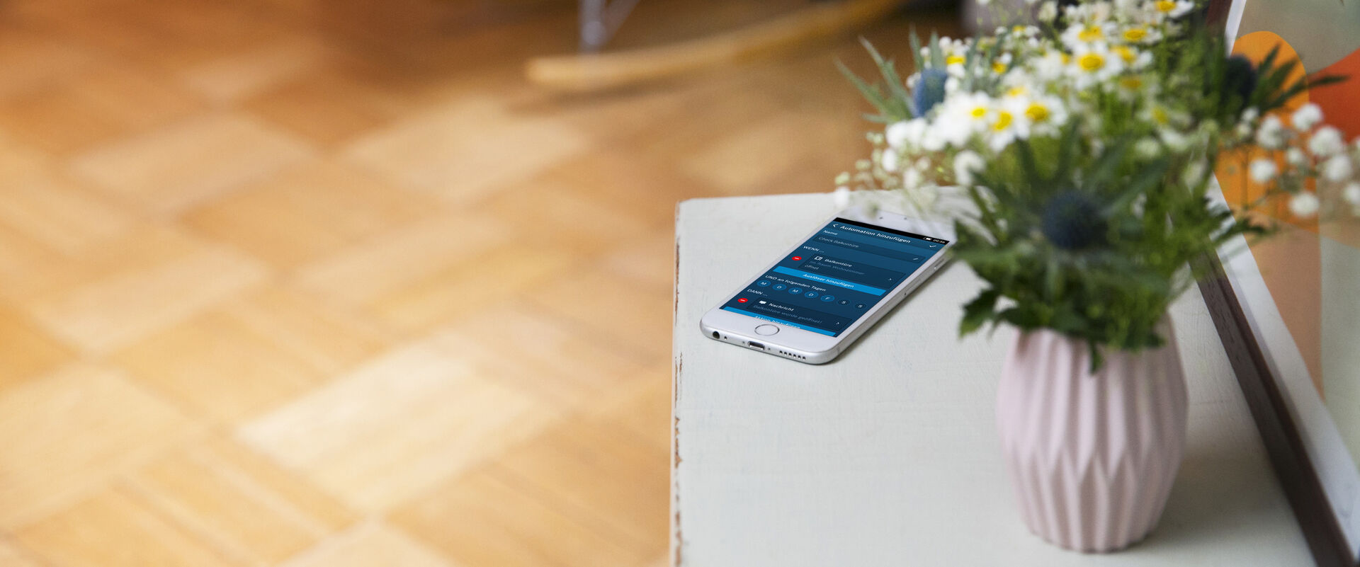 Ablage mit Smartphone und einer rosa Blumenvase mit bunten Blumen.