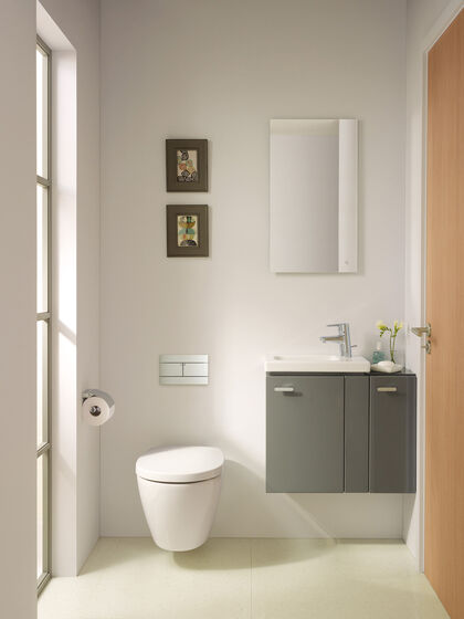 Toilette für Gäste wandmontiert und Waschplatz mit grauem Badmöbel und Spiegel.