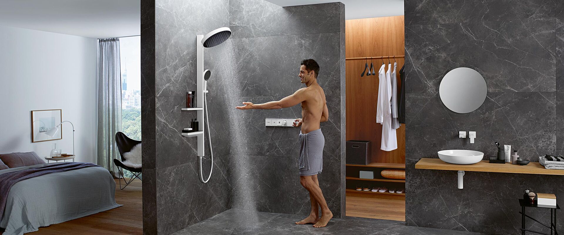Offenes Badezimmer mit Schlafzimmer und Ankleide und im Zentrum der Duschbereich, ausgestattet mit den Rainfinity Brausen von hansgrohe – hier mit Showerpipe und Mann.