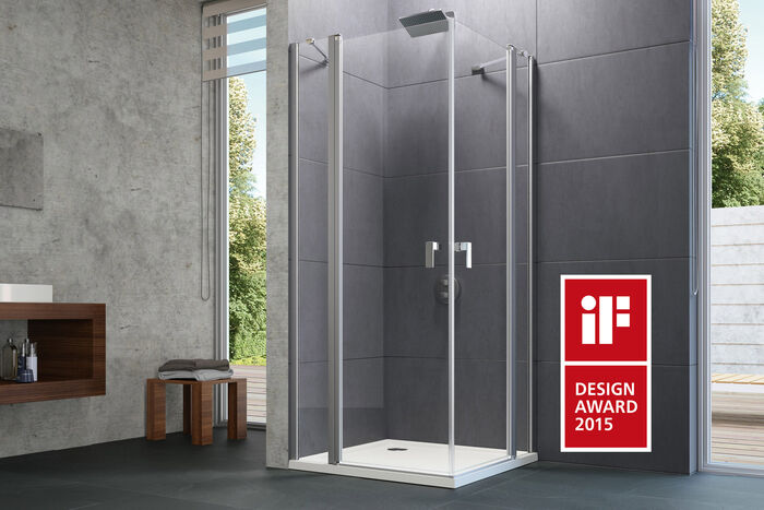 Badezimmer, in dem die Design Pure Duschabtrennung von HUEPPE installiert ist. Links ist ein Waschbeckenunterschrank zu erkennen, daneben ein Stuhl, auf dem Handtücher liegen. Rechts befindet sich das Logo eines Designpreises.