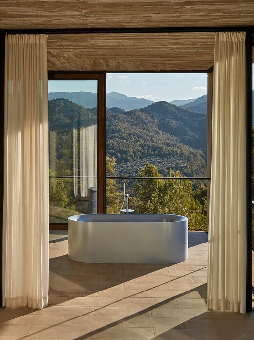 Mediterranes, offenes Bad mit Vorhängen und Aussicht, in dessen Mittelpunkt die BetteLux Oval Silhouette Badewanne steht. Besonderes Highlight: Ausführung in Satin Blue Effektfarbe.