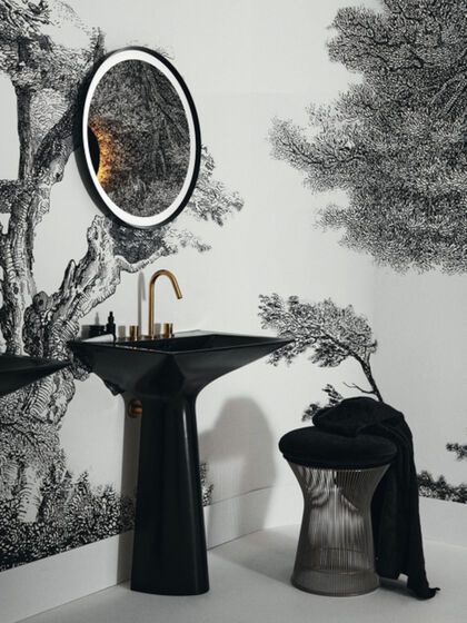 Der schwarze, monolithische Waschtisch Tipo-Z von Ideal Standard kombiniert mit einem Spiegel mit schwarzer Umrandung und einem schwarzen Hocker, dazu goldenen Armaturen. 