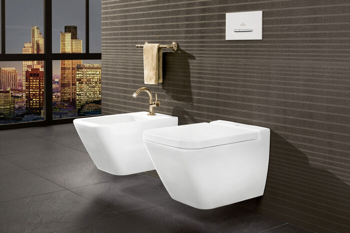 Bidet mit Armatur in Gold neben Toilette wandmontiert.