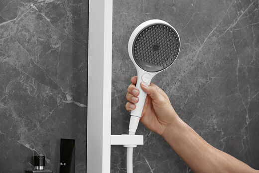 Detailbild der runden Handbrause Rainfinity in matt weiß von hansgrohe – mit Hand, die die Brause abnimmt.