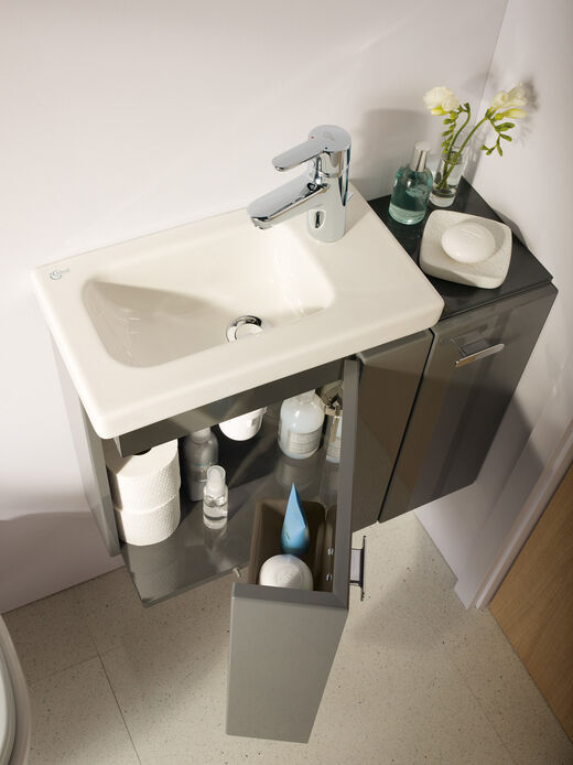 Handwaschbecken mit kleiner Ablage und geöffnetem Unterschrank mit Stauraum für Handtücher und Türe, um etwas einzustellen.