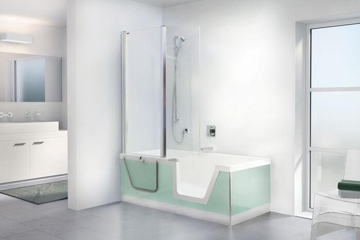 Badezimmer mit-Badewanne mit Eintieg in mint. Duschwand und Handbrause mit Stange an der Wand. Doppelwaschtisch im Hintergrund