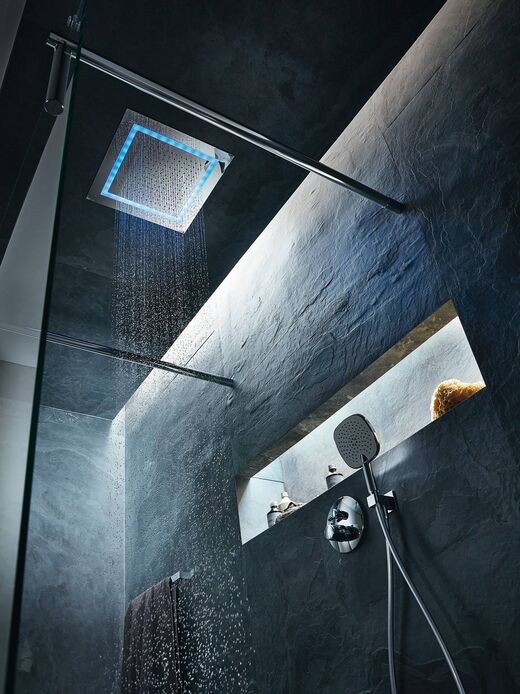 Blick von unten an die Decke in einer Dusche. Man sieht das beleuchtete Duschpaneel bei laufendem Wasser, eine beleuchtete Nische/Ablage und eine Handbrause.