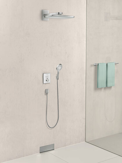 Beige geflieste bodenebene Dusche mit hansgrohe Rainmaker Select Kopfbrause. Hinter einer Glasscheibe sind zwei turkiese Handtücher zu erkennen.